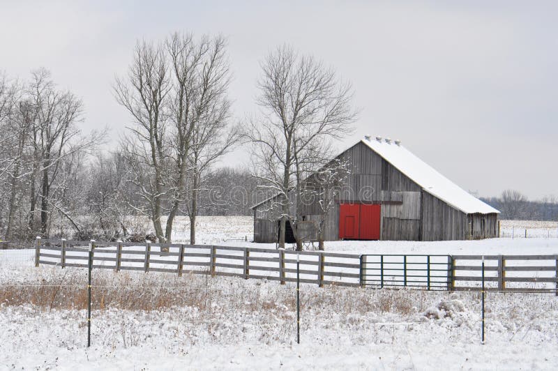 Gray Country Barn With a Red Door on a Snow Covered Landscape