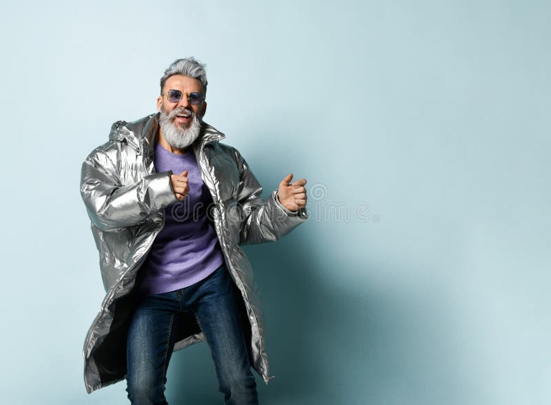Mature man in purple pullover, sunglasses, silver colored down jacket, jeans. Running, posing on blue background. Gray-haired, bearded, mature man in purple stock images Mature man in purple pullover, sunglasses, silver colored down jacket, jeans. Running, posing on blue background. Gray-haired, bearded, mature man in purple stock images