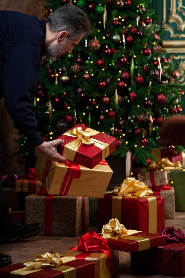 Gray-haired man lays out gifts near decorated New Year tree royalty free stock image