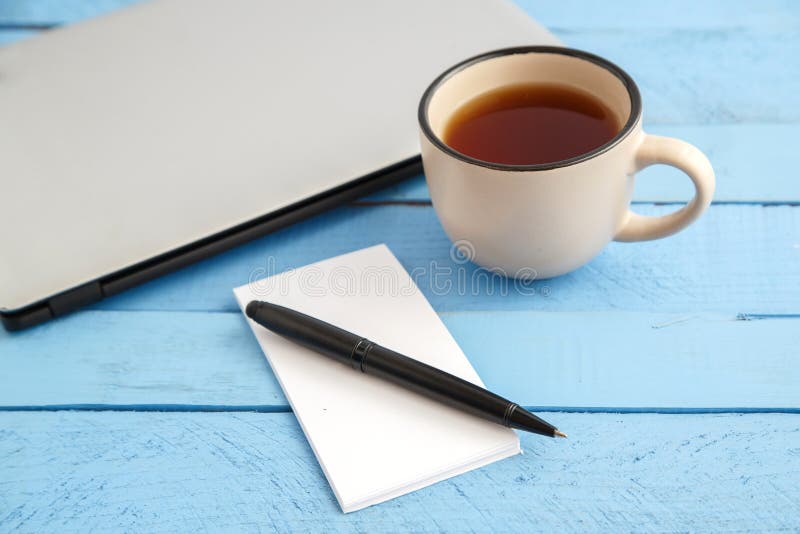 A Gray Laptop, A Cup Of Drink,a Small Paper Notebook And A Black Pen On A Blue Wooden Background. The View From The Top