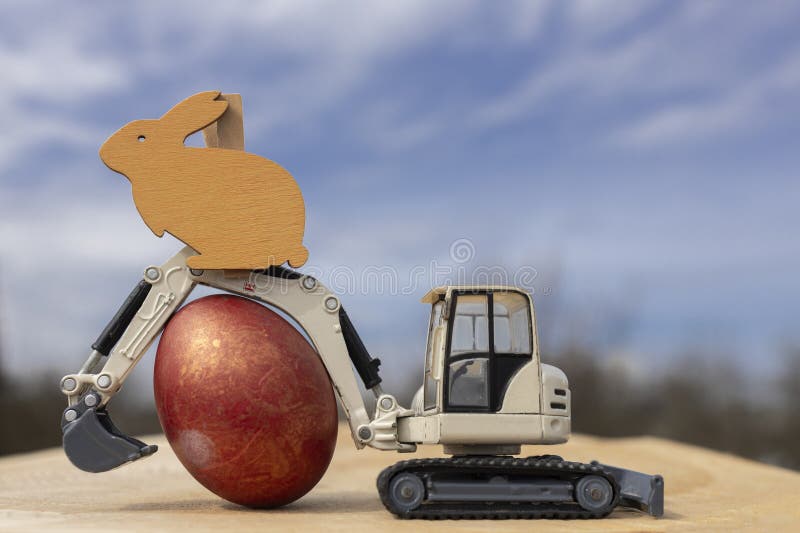 gray small toy excavator and an Easter egg against the sky. Easter holiday concept