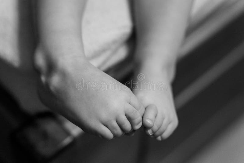 Grayscale Shot of a Child S Legs Play with Each Other Stock Photo