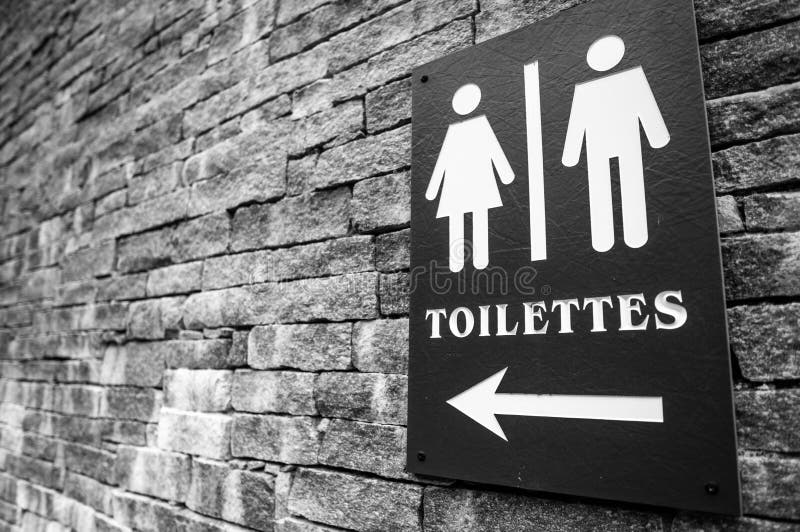 Grayscale shot of a toilet arrow sign on a brick wall stock images