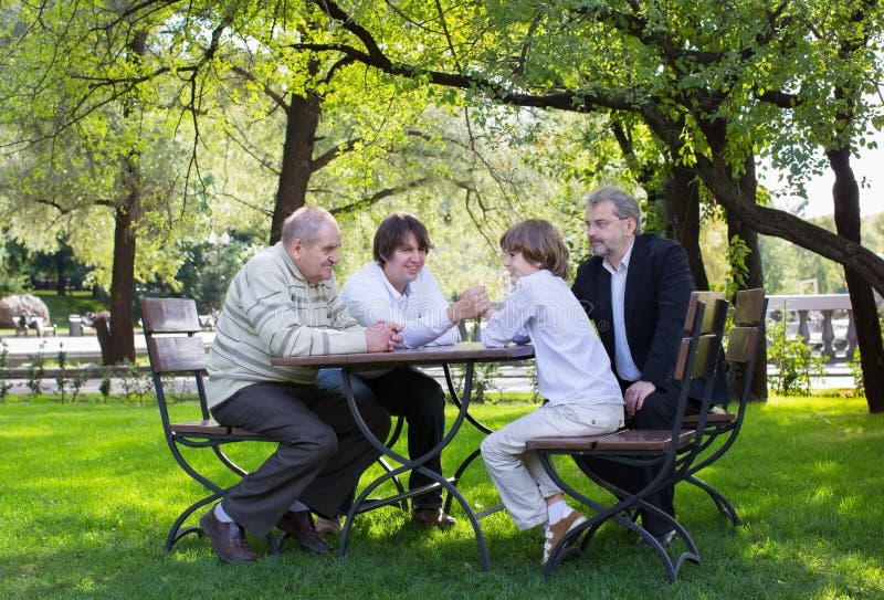 Great-grandfather, grandfather, father and son wrestling at a wooden table in a park