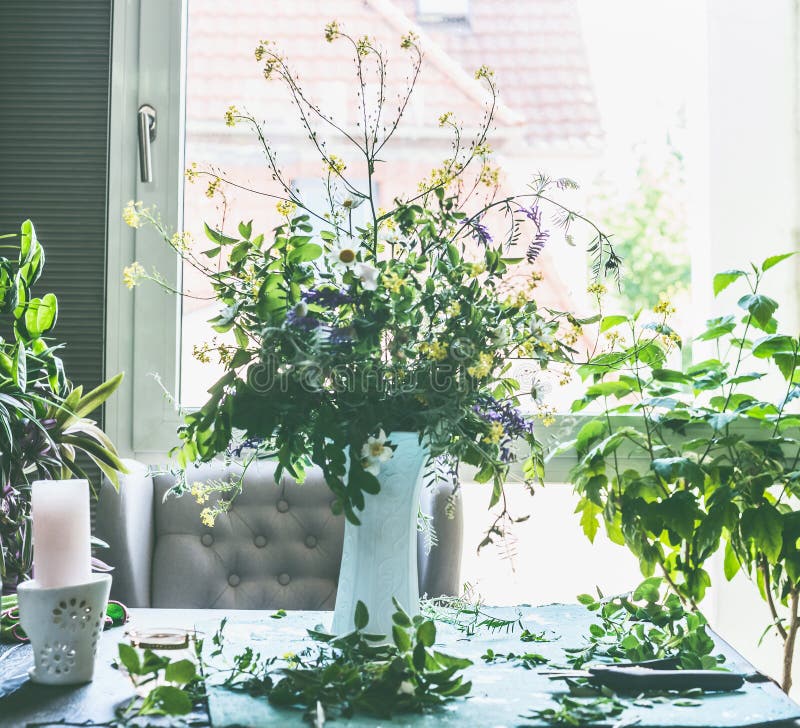 Great summer wild flowers bunch in white vase on table in living room at window . Home lifestyle