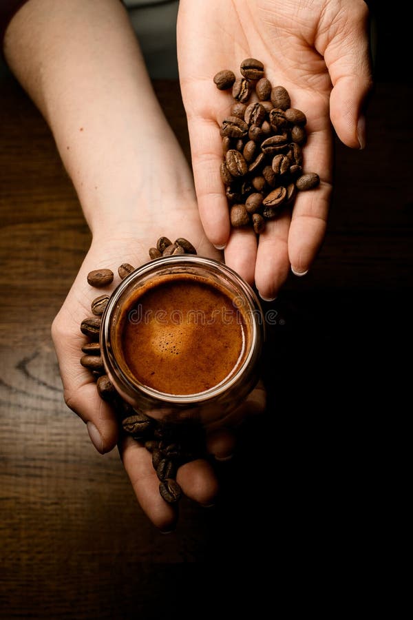 Great top view on hands holding coffee beans and cup of coffee over wooden surface