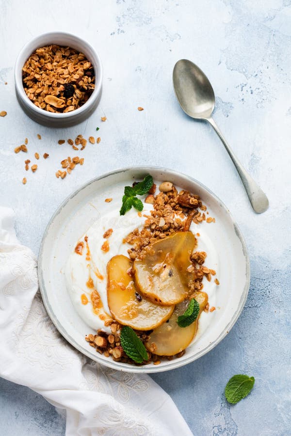 Greek yogurt with caramelized pear, granola, nuts and melted sugar for a wholesome breakfast on a gray ceramic plate. Rustic style. Top view