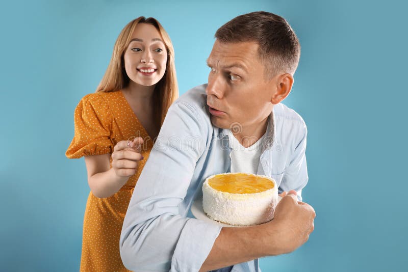 Greedy man hiding tasty cake from woman on turquoise background royalty free stock photos
