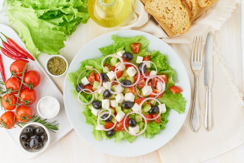 Greek salad on white plate on old rustic white wooden table, fresh salad with tomatoes, cucumbers, feta, onion. Top view