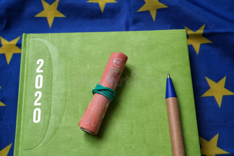A green agenda with writing, 2020,some banknotes and a blue pen on a flag of the European Union