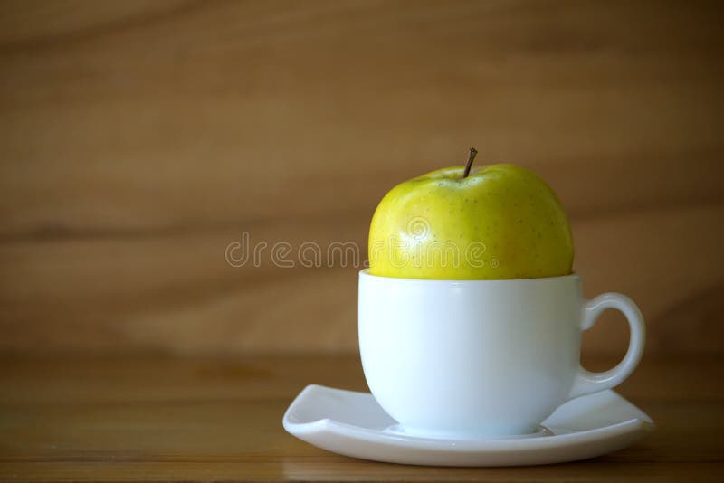 Green apple and white cup on wooden table over wooden background