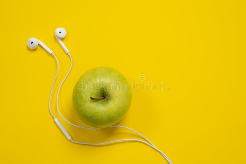 Green Apple and White Wired Headphones on a Bright Yellow Background