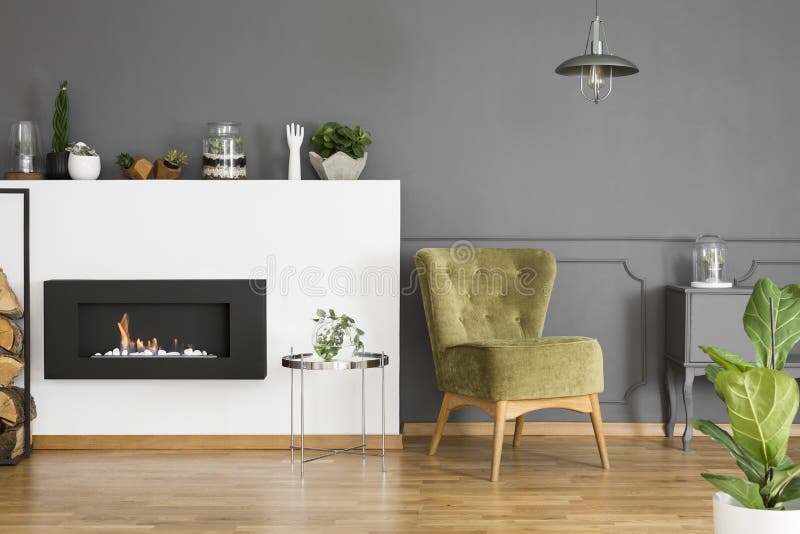 Green armchair and silver table next to fireplace in grey apartment interior with plant. Real photo royalty free stock photo Green armchair and silver table next to fireplace in grey apartment interior with plant. Real photo royalty free stock photo
