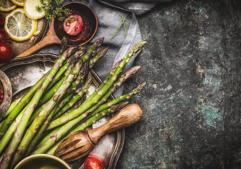 Green asparagus cooking preparation with cooking spoon and ingredients on rustic background, top view