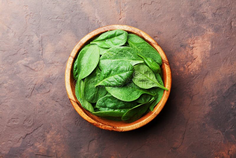 Green baby spinach leaves in wooden bowl on rustic stone table top view. Organic healthy food. stock image Green baby spinach leaves in wooden bowl on rustic stone table top view. Organic healthy food. stock image