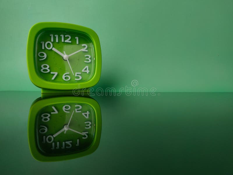 Green clock on green background with reflection on a black acrylic board royalty free stock photography
