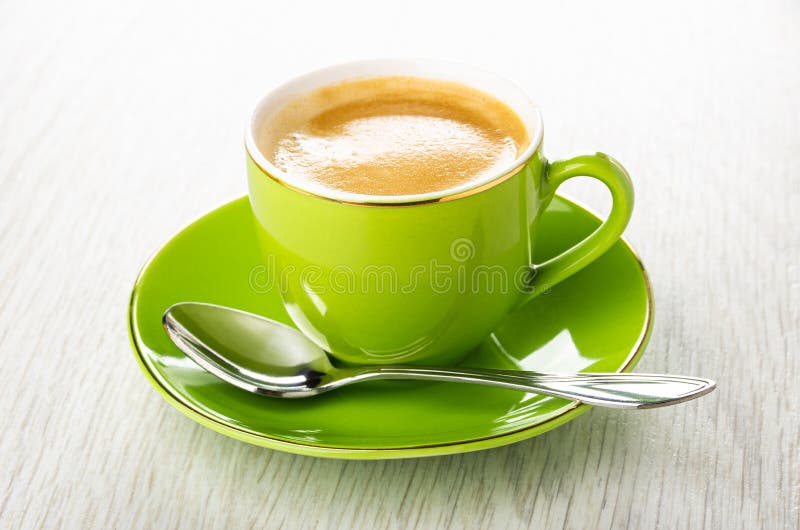 Green cup with coffee, spoon on saucer on wooden table