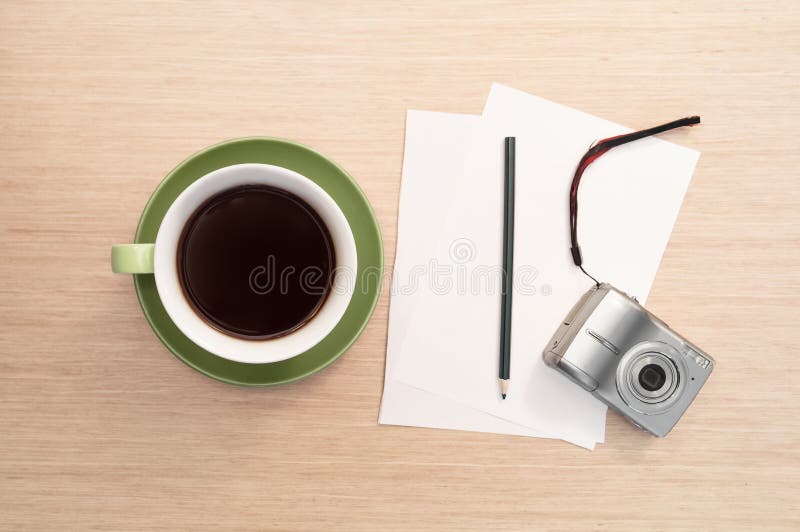 A green cup of coffee on the table and empty sheet, pencil, camera