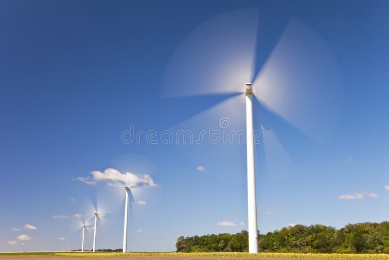 A farm of wind turbines or windmills providing alternative sustainable green energy, situated in a field of sunflowers. A farm of wind turbines or windmills providing alternative sustainable green energy, situated in a field of sunflowers