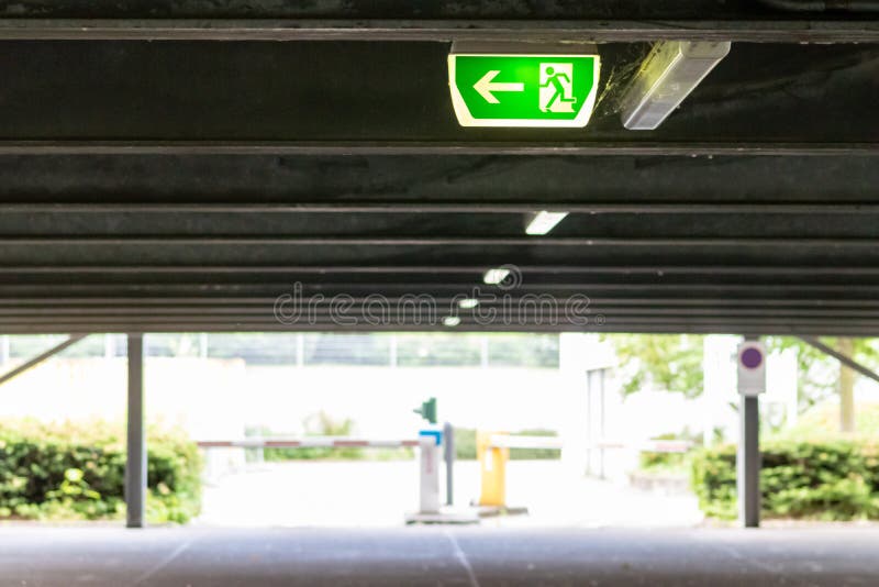Green exit sign with running person and green arrow shows guidance system signage in a parking lot for rescue evacuation safety stock photography