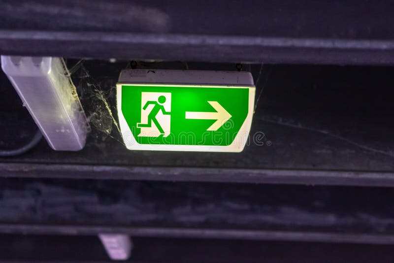 Green exit sign with running person and green arrow shows guidance system signage in a parking lot for rescue evacuation safety stock images