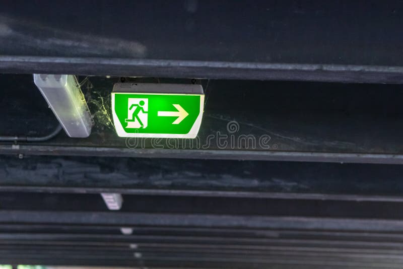 Green exit sign with running person and green arrow shows guidance system signage in a parking lot for rescue evacuation safety stock image