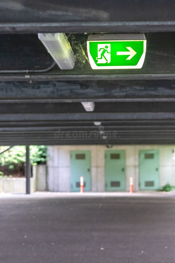 Green exit sign with running person and green arrow shows guidance system signage in a parking lot for rescue evacuation safety stock photo