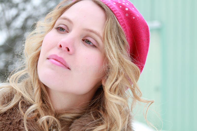 Portrait of a slightly smiling, wholesome, beautiful, green eyed young woman wearing a fur jacket and pink beret with snowy tree and building in background. Portrait of a slightly smiling, wholesome, beautiful, green eyed young woman wearing a fur jacket and pink beret with snowy tree and building in background.