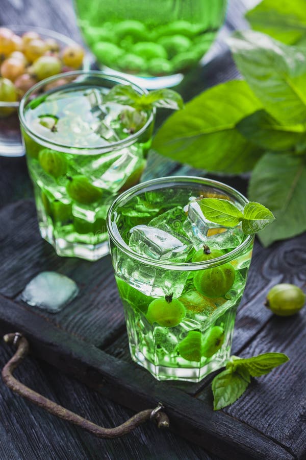 Green gooseberry cocktail with ice and fresh mint on a black wooden table