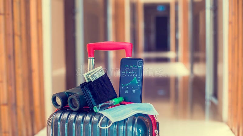 Green graph on smartphone with medicine mask, wallet, Dollar, Binoculars and travel equipment on luggage in hotel