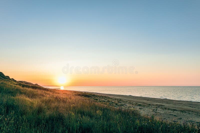 Green hill and sandy beach at sunset. Evening sea landscape with low sun on horizon. Peresyp resort village, Krasnodar region, Russia royalty free stock image Green hill and sandy beach at sunset. Evening sea landscape with low sun on horizon. Peresyp resort village, Krasnodar region, Russia royalty free stock image
