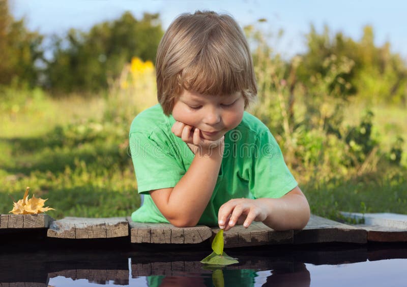 Green leaf-ship in children hand in water, boy in park play with