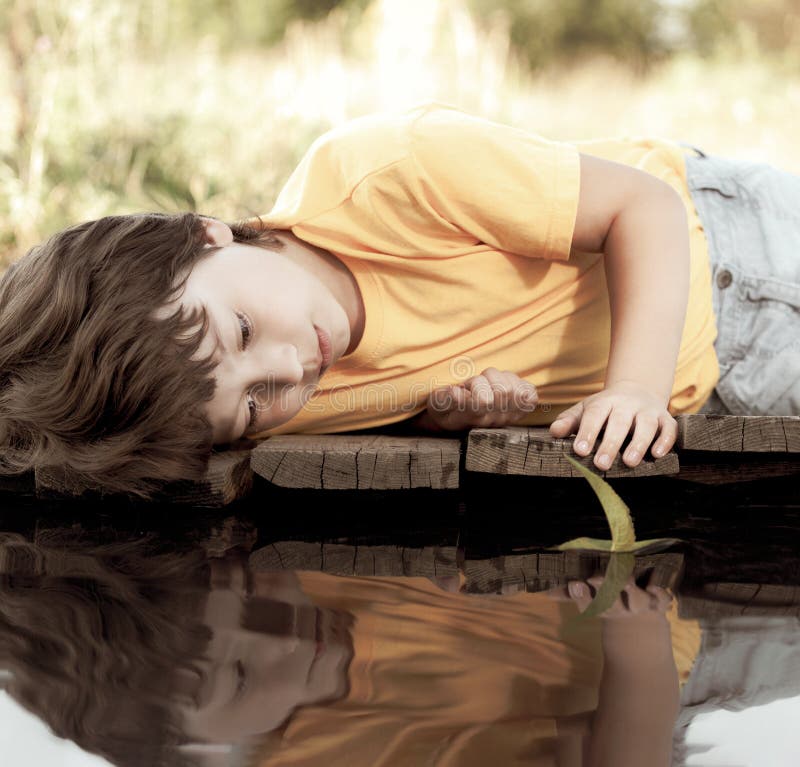 Green leaf-ship in children hand in water, boy in park play with boat in river