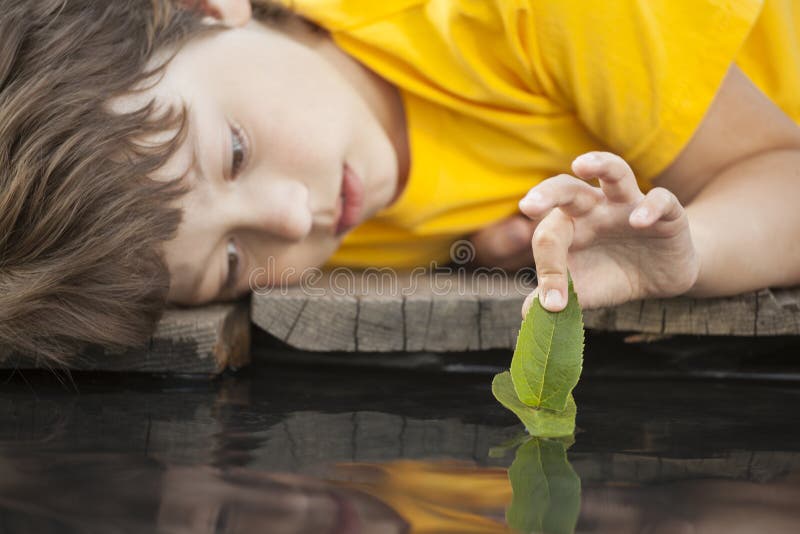 Green leaf-ship in children hand in water, boy in park play with