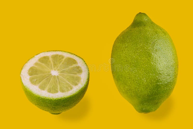 Green lemon of Siracusa, Sicilia, Italy, femminello variety, one whole fruit and one half cut isolated on yellow background, copy space. Green lemon of Siracusa, Sicilia, Italy, femminello variety, one whole fruit and one half cut isolated on yellow background, copy space
