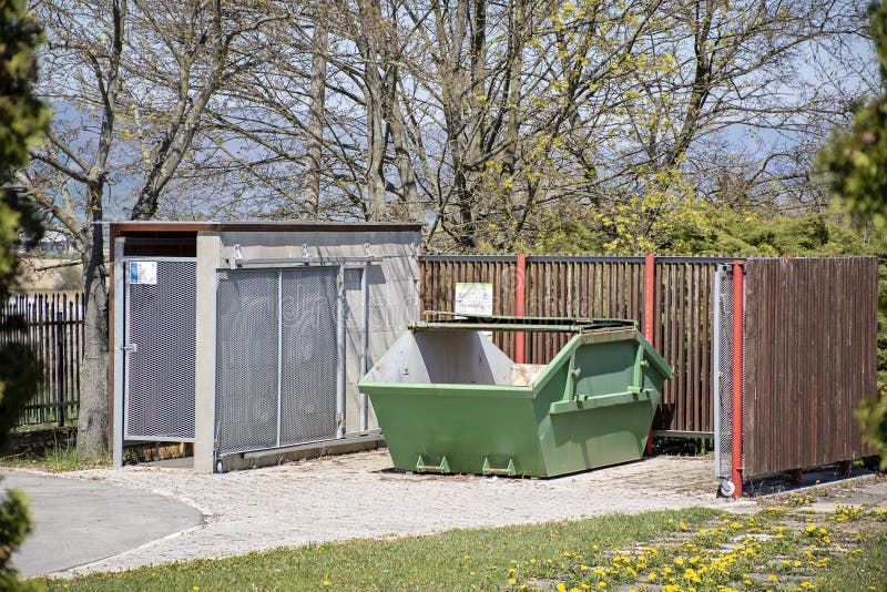Green metal skip. Industrial rubbish skip in front of wooden fence. Rubbish place. Empty dumpster