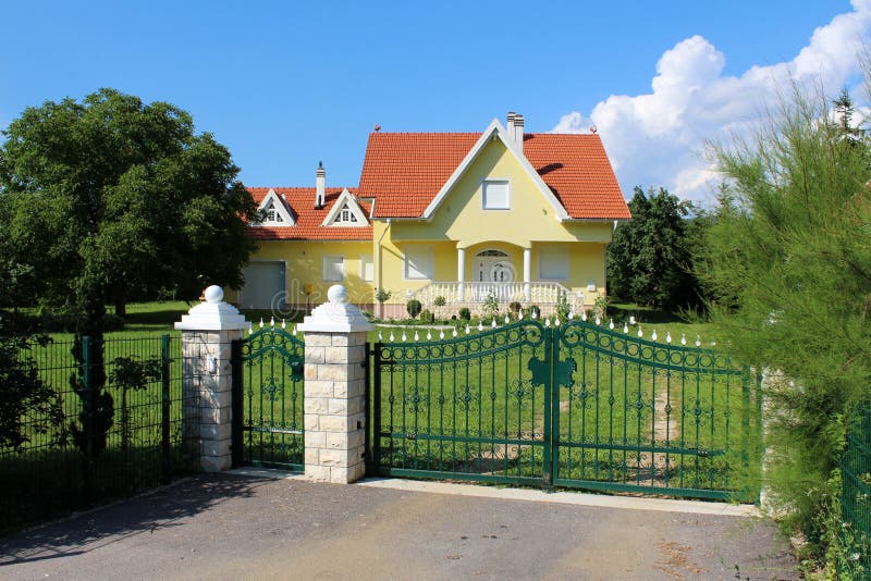 Green metal wrought fence with stone pillars in front of modern suburban family house with garage royalty free stock images Green metal wrought fence with stone pillars in front of modern suburban family house with garage royalty free stock images