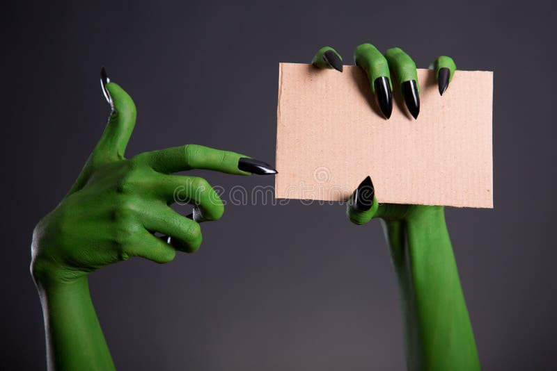 Green monster hand with black nails pointing on blank piece of c