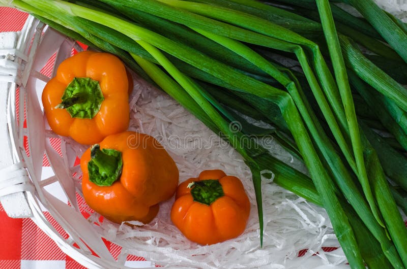 Green onion and sweet colored pepper in white wooden basket with straw