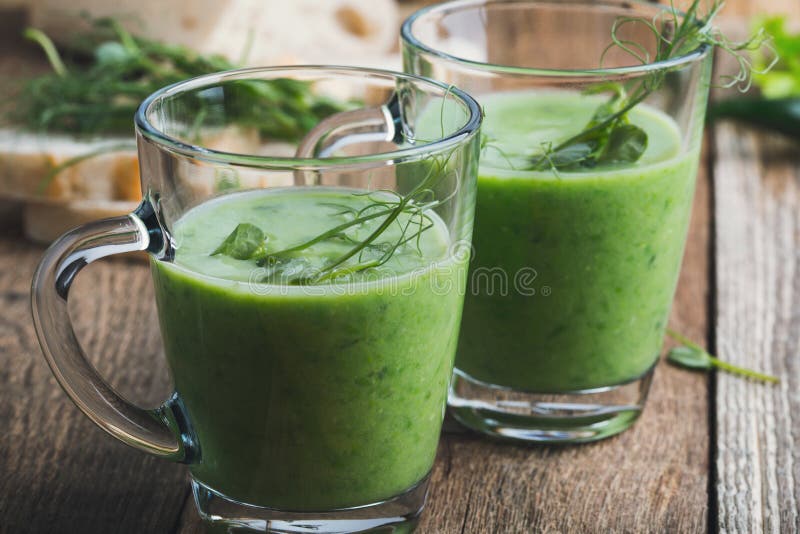 Green pea soup in glass mug with sprouts on top on wooden rustic table, healthy vegan plant-based meal