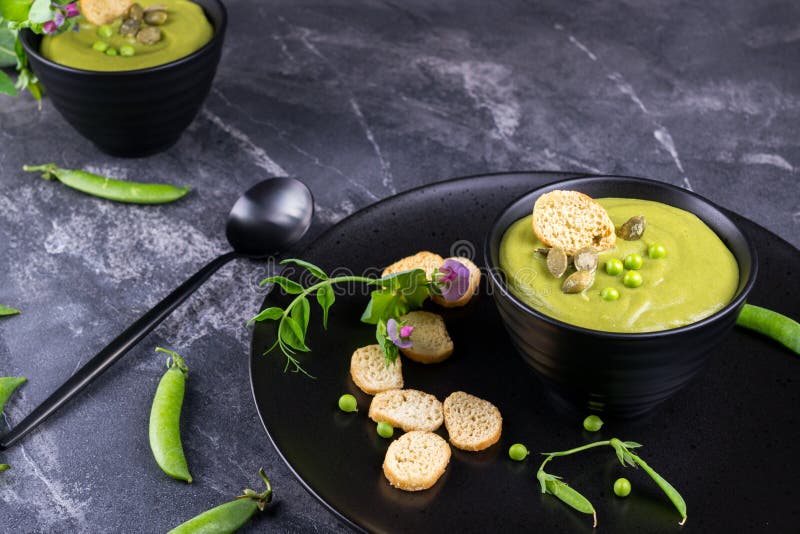 Green pea soup puree with croutons in black bowl. On dark stone