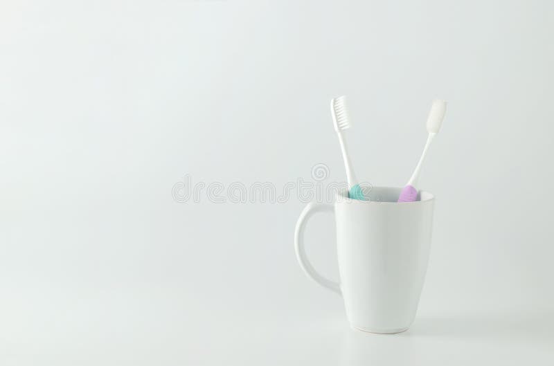 Green and purple toothbrush with white ceramic mug on white back stock photography