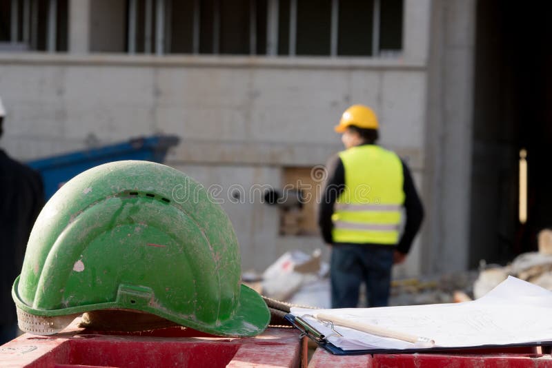 Green safety hardhat on foreground. Construction worker on background stock photography Green safety hardhat on foreground. Construction worker on background stock photography