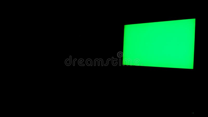 Green screen isolated on black background. TV with glowing chroma key hanging on the black wall in the room at night. Green screen isolated on black background. TV with glowing chroma key hanging on the black wall in the room at night.