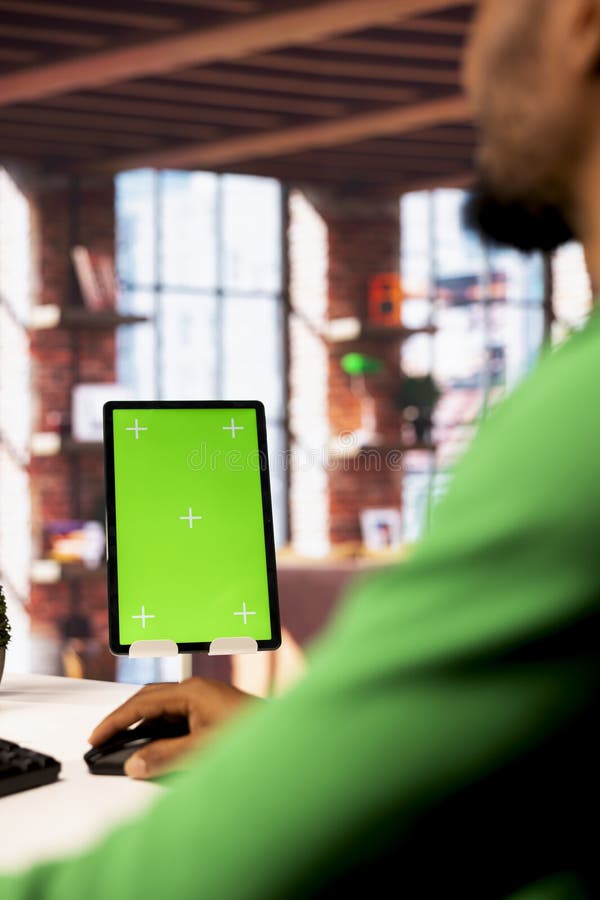 Green screen tablet on desk next to man in home office typing on PC royalty free stock photography