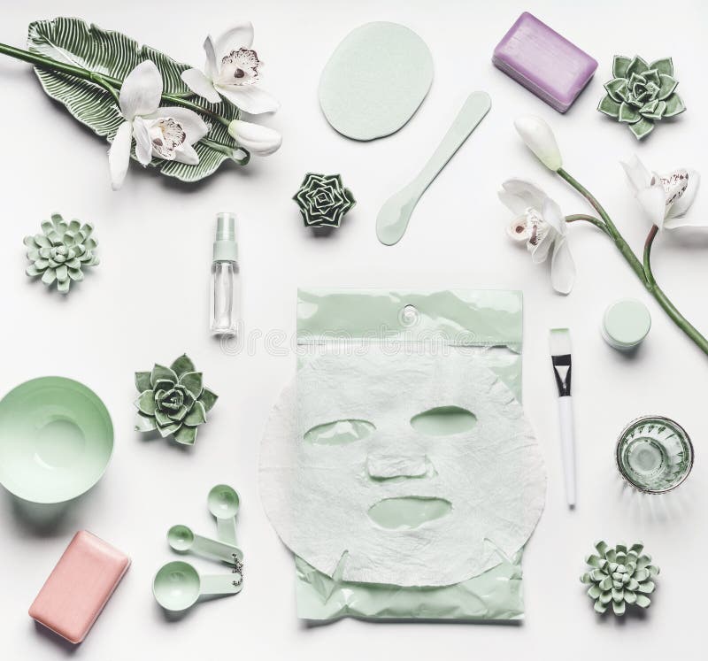 Green skin care cosmetic setting with orchid flowers, accessories and facial calming sheet mask on white background, top view, frame, flat lay. Beauty concept