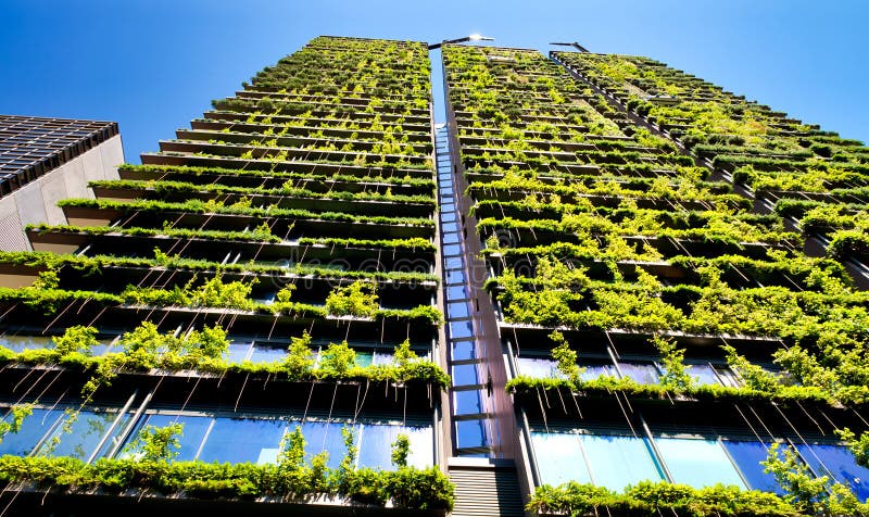 Green skyscraper building with plants growing on the facade against blue sky. Ecology and green living in city, urban environment stock image Green skyscraper building with plants growing on the facade against blue sky. Ecology and green living in city, urban environment stock image