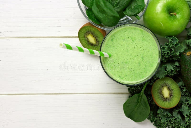 Green smoothie above view with ingredients against white wood