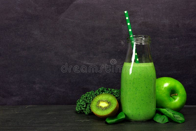 Green smoothie in a milk bottle with ingredients against slate