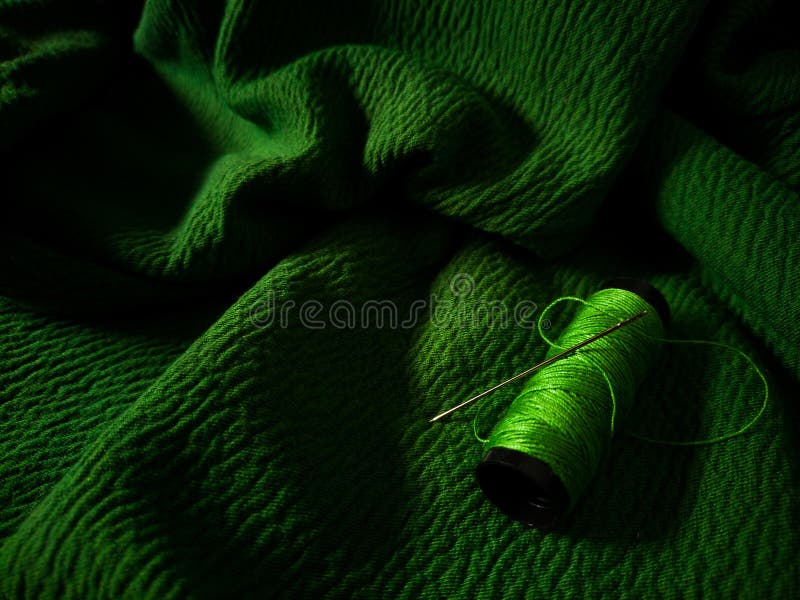 Green thread spool lies on a green textured fabric royalty free stock image